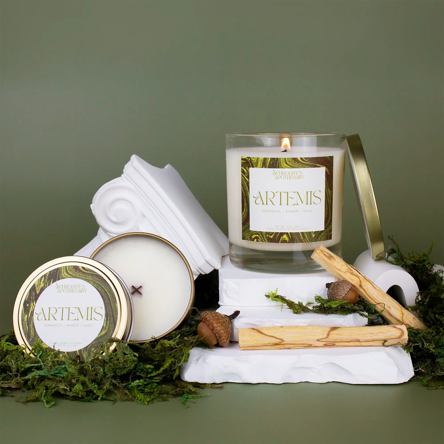 Artemis Candle 8.5 oz and Artemis 4 oz candle on a Greek themed photo set with moss