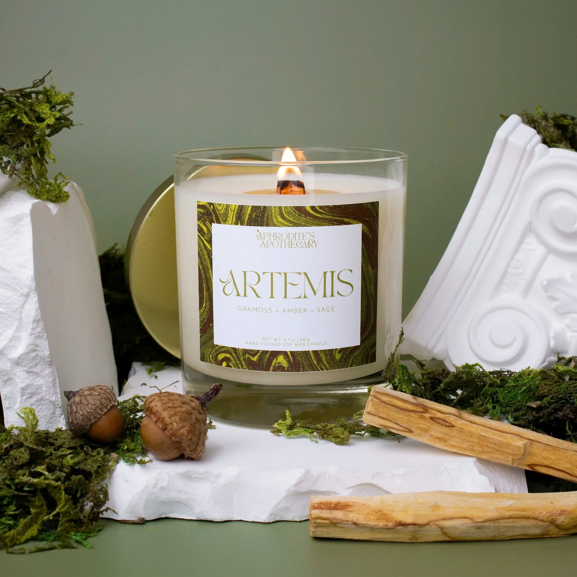 Close up of Artemis Candle 8.5 oz on Greek themed photo set with moss