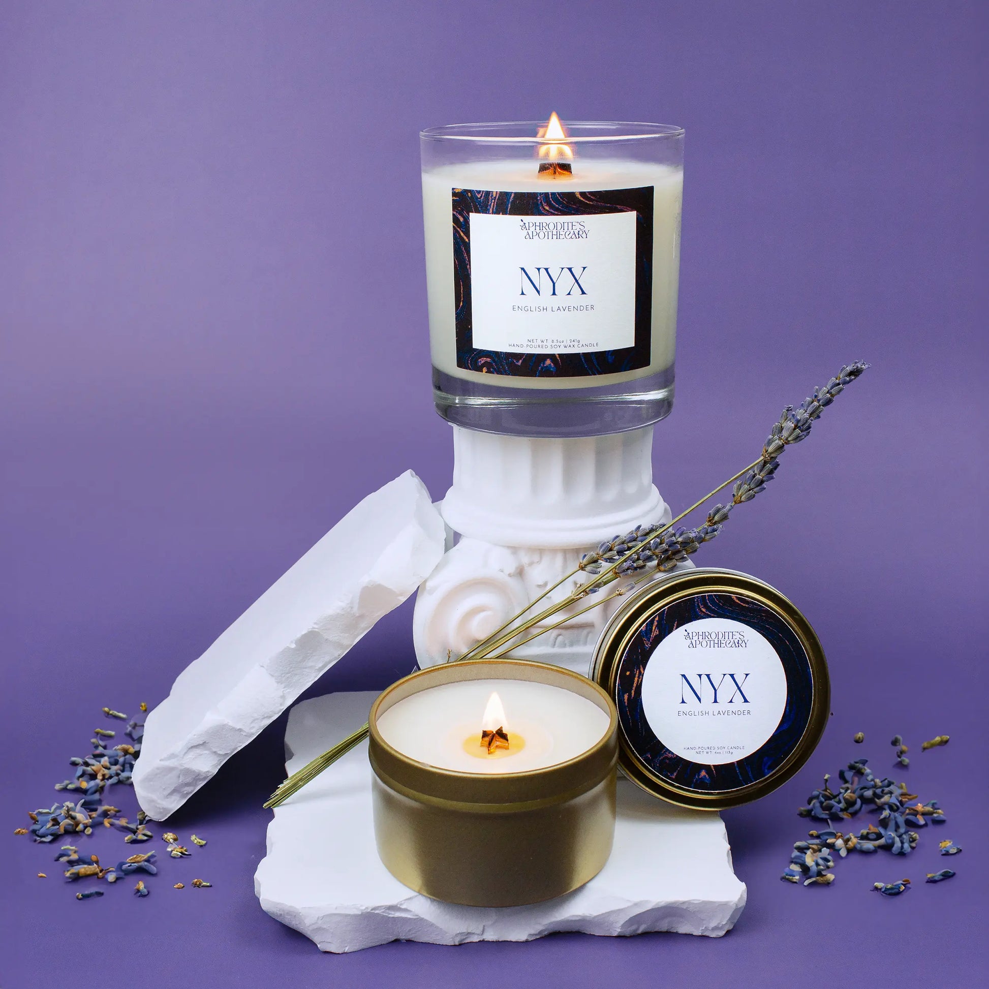 Nyx Candle 8.5 oz and Nyx Candle 4 oz on Greek ruin themed photo set with lavender flowers on a lavender background.