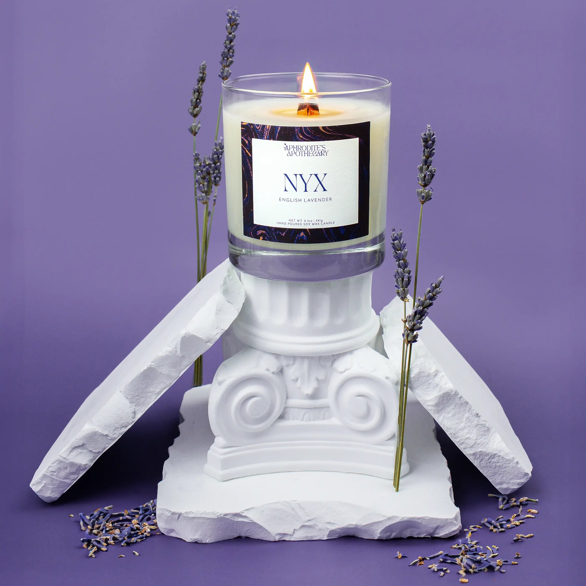 Nyx Candle 8.5 oz on Greek ruin themed photo set with lavender flowers on a lavender background.