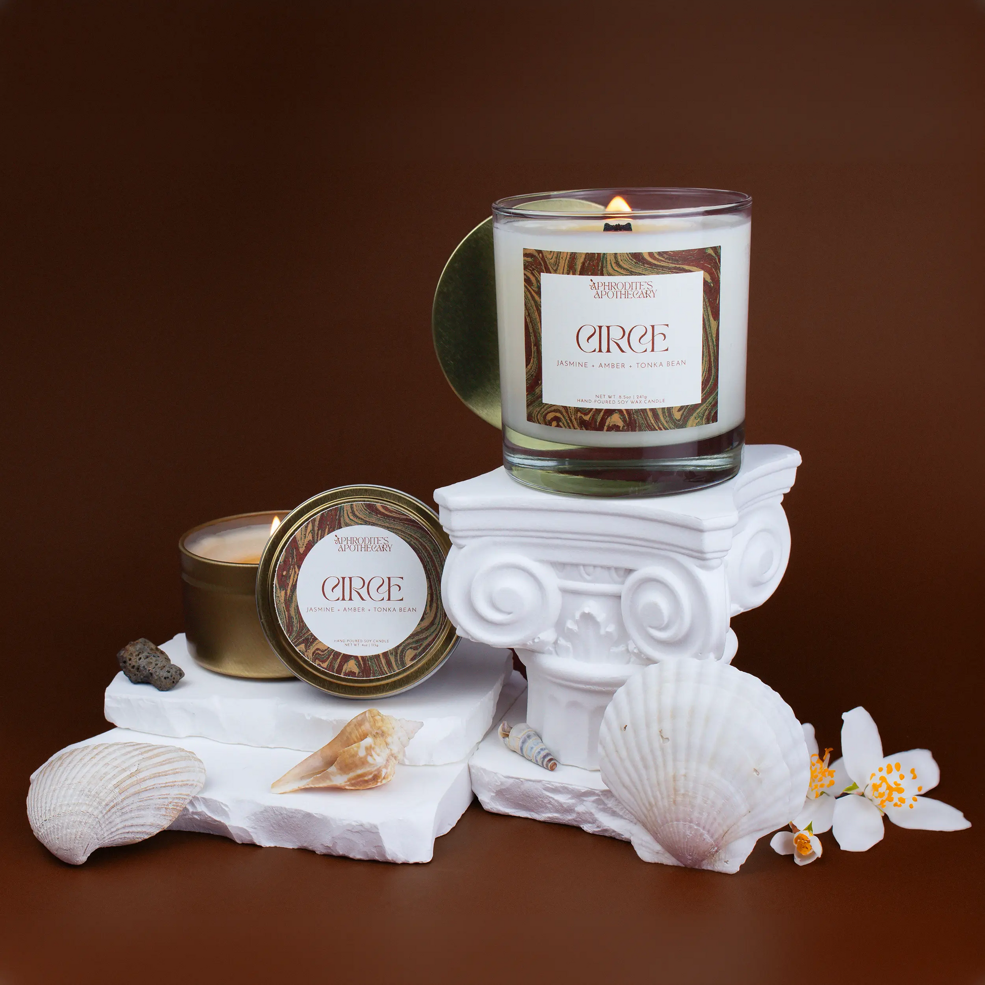 Circe Candle 8.5 oz and Circe Candle 4 oz on Greek themed photo set with jasmine flowers, seashells, and beach rocks