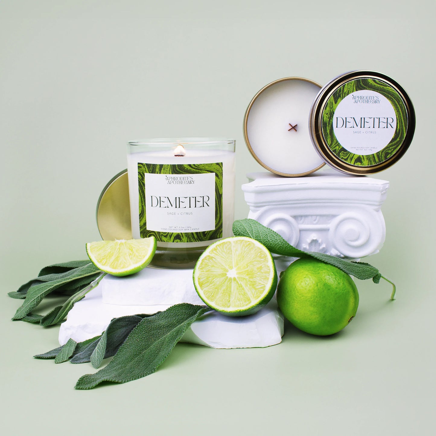 Demeter Candle 8.5 oz and Demeter Candle 4 oz on Greek themed photo set with sliced limes and sage leaves on a soft green background