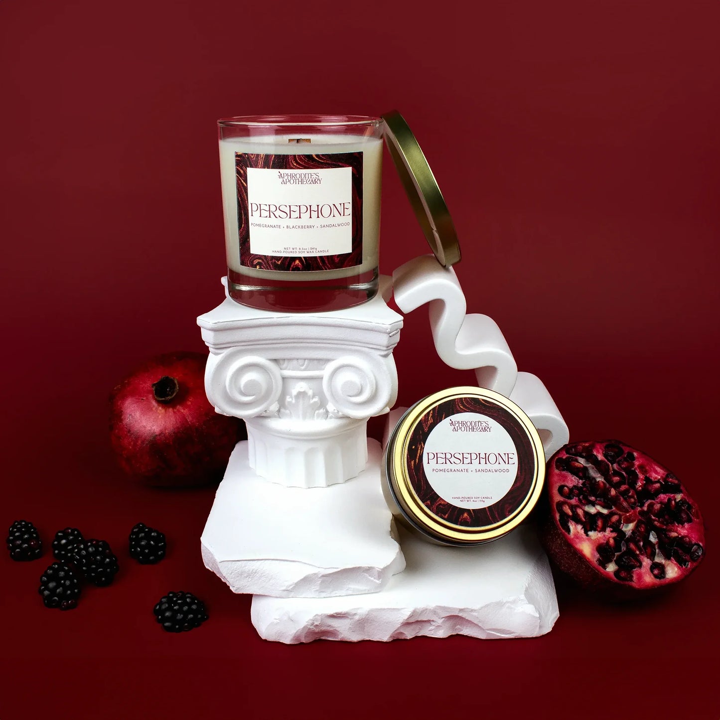 Persephone Candle 8.5 oz and Persephone Candle 4 oz on a Greek themed photo set with pomegranates and pomegranate seeds, and blackberries on a deep red background.