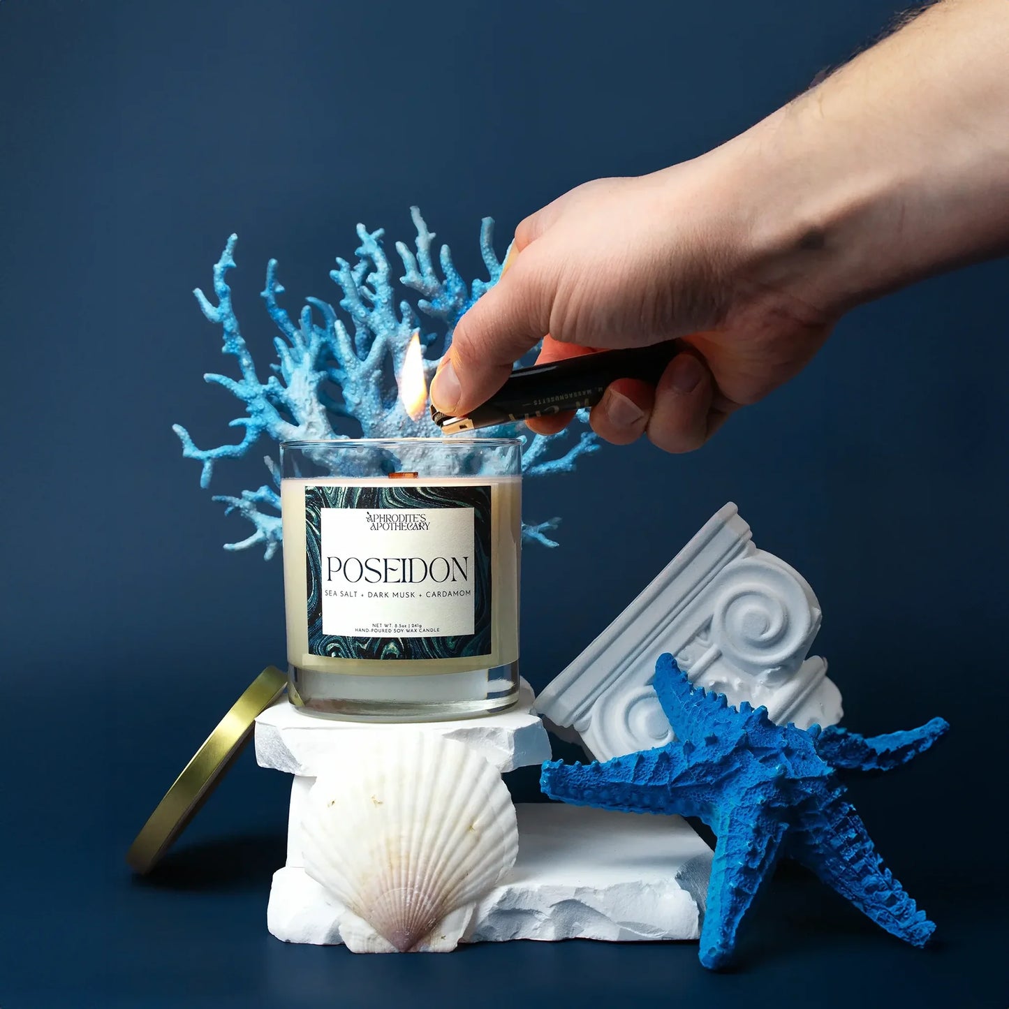 Poseidon Candle 8.5 oz being lit on an underwater Greek themed photo set with starfish and coral on a blue background.