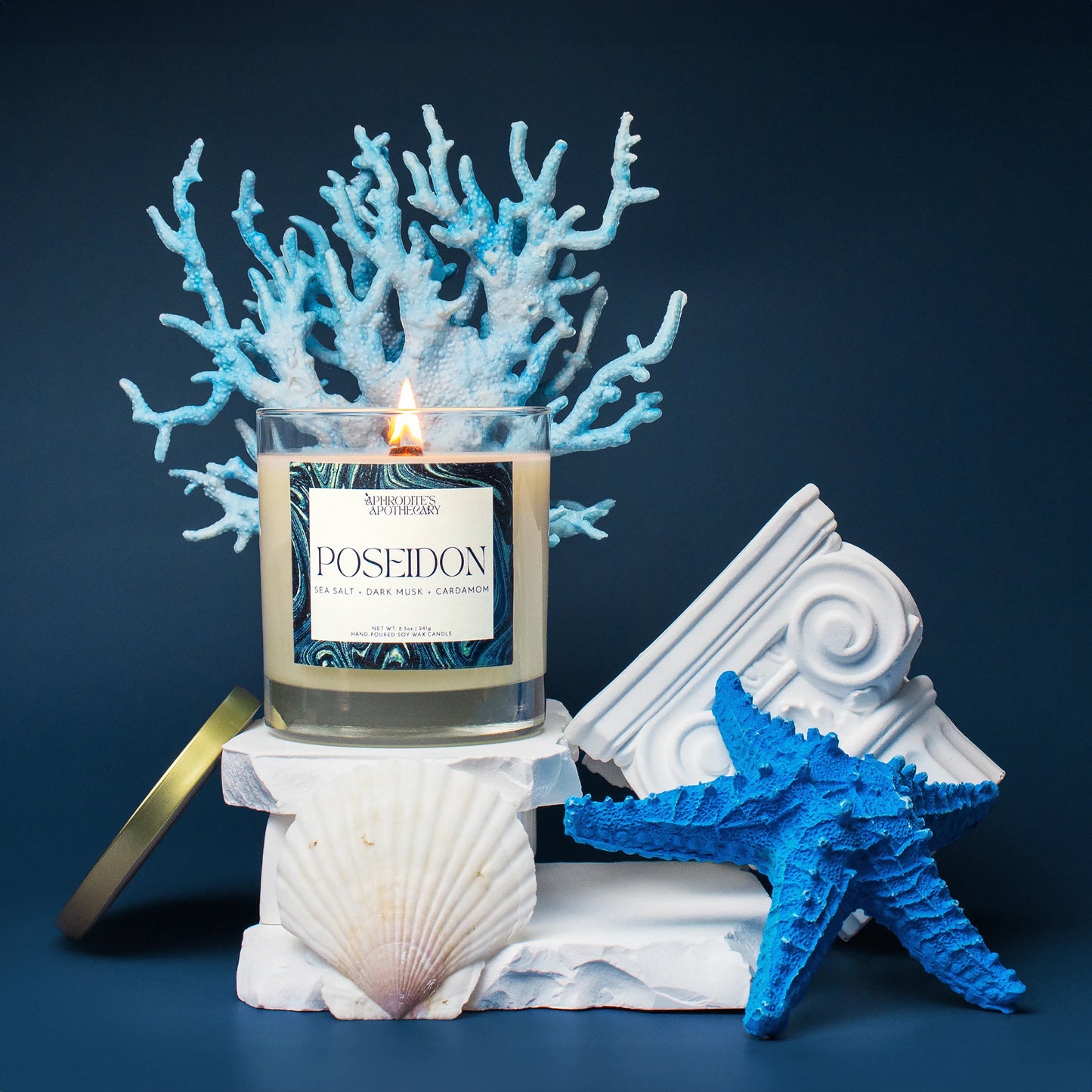 Poseidon Candle 8.5 oz on an underwater Greek themed photo set with starfish and coral on a blue background.